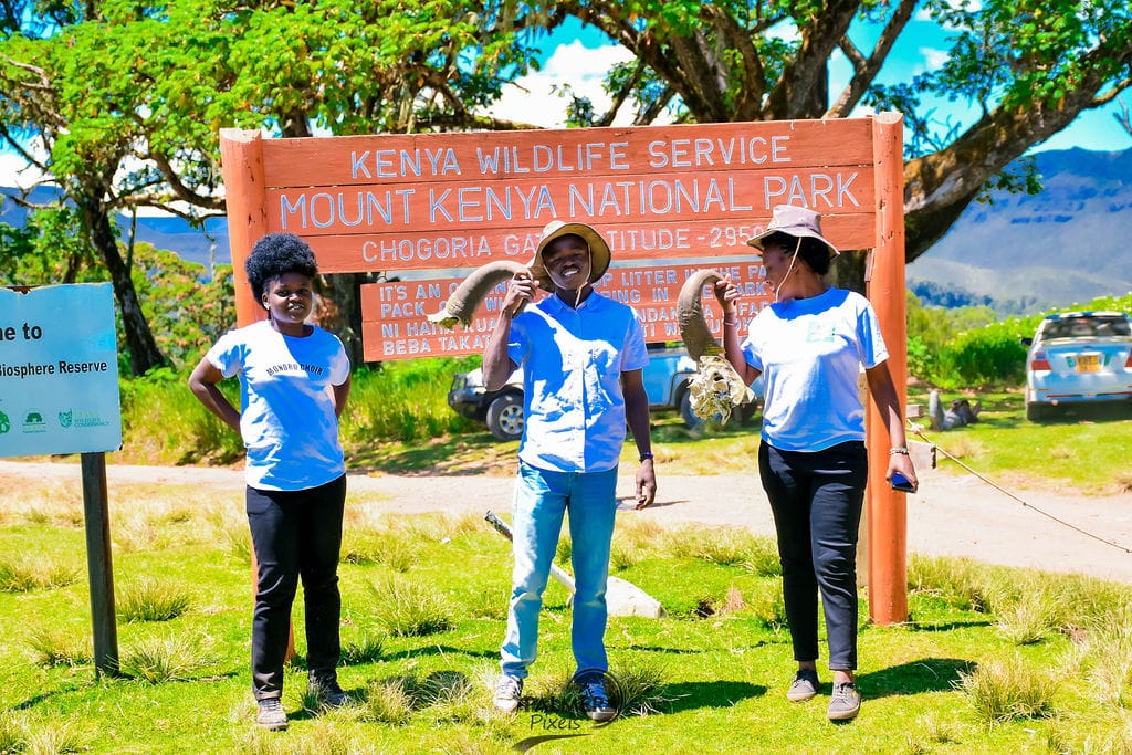 Three people pose at the Mount Kenya National Park entrance sign